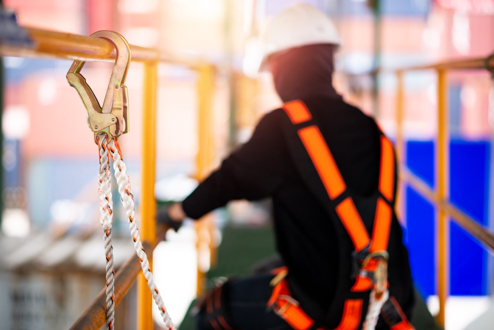 A worker wearing a fall-arrest safety harness clipped to scaffolding at height