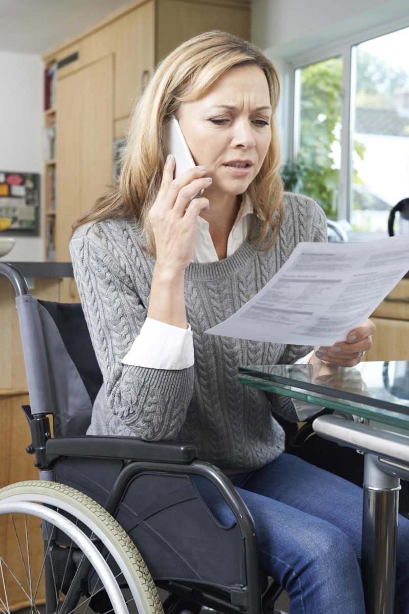 A woman using a wheelchair reviews a benefits letter while speaking on the phone at home